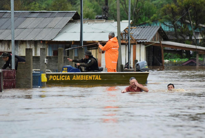 Agentes de policía revisan una casa mientras habitantes vadean una calle inundada por tormentas derivadas de un ciclón en Passo Fundo, en el estado de Rio Grande do Sul.