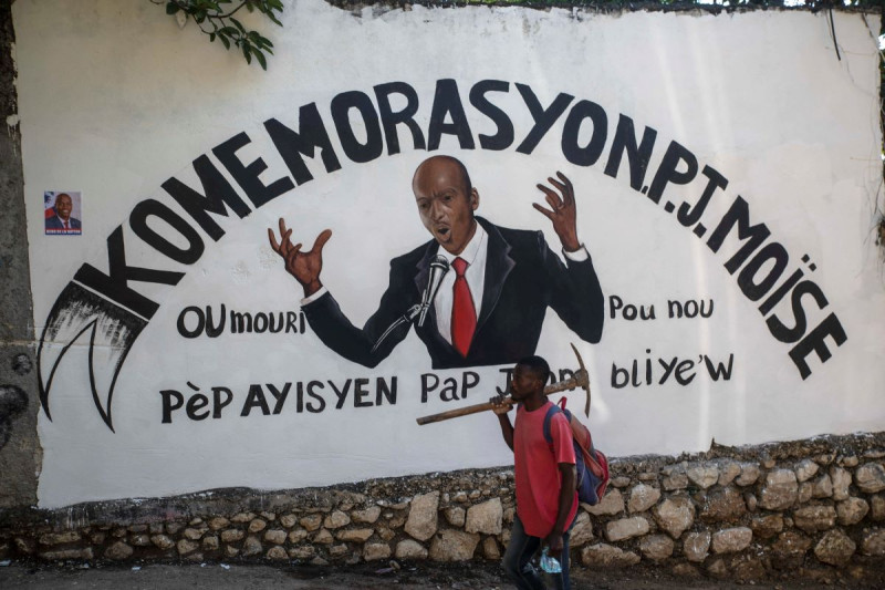 Un hombre con un pico pasa por delante de un mural en honor al presidente asesinado Jovenel Moïse, que dice en criollo “conmemoración para el presidente Moïse”, cerca de la exresidencia presidencial.