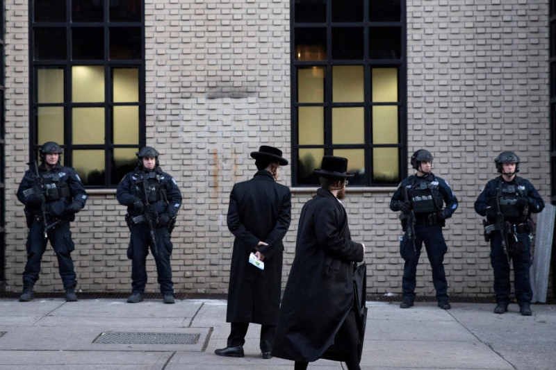 Judíos ortodoxos pasan junto a policías que custodian una sinagoga en Brooklyn el 11 de diciembre de 2019, en Nueva York.