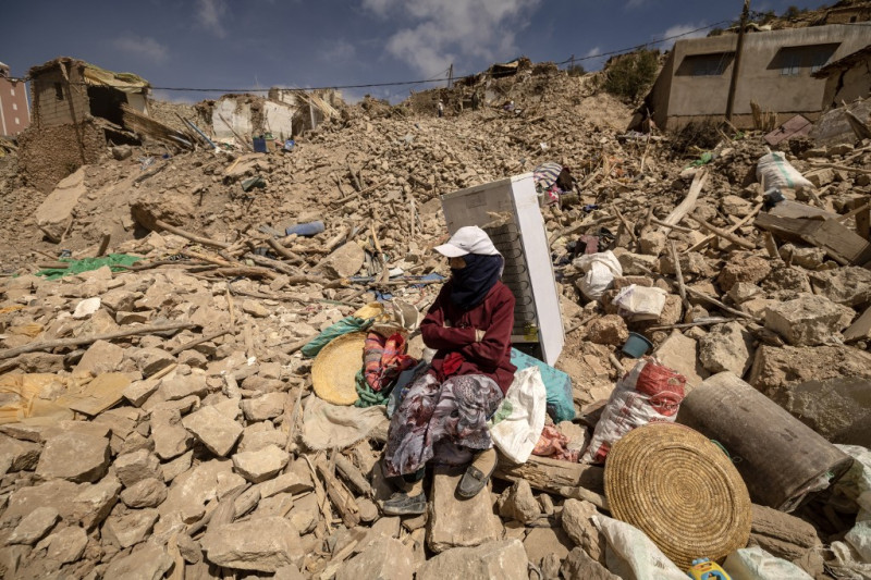 Una mujer sentada junto a un refrigerador y otros artículos rescatados en medio de los escombros en la aldea de Douzro