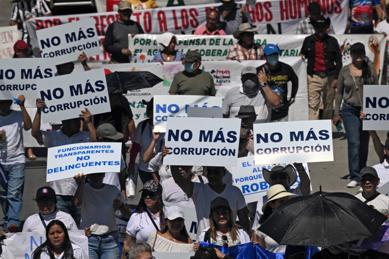 La gente porta carteles que dicen "No más corrupción" durante una protesta contra las políticas del presidente Nayib Bukele y su reelección el Día de la Independencia en San Salvador
