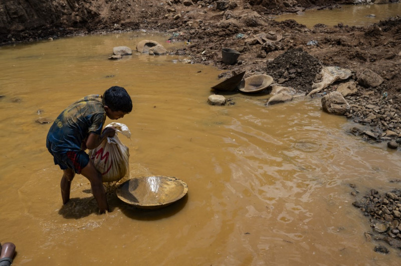 Un niño minero venezolano descarga una bolsa de barro en un contenedor de madera utilizado para colar y lavar el barro en busca de oro en una mina a cielo abierto, que luego se venderá en El Callao, estado de Bolívar, Venezuela, el 29 de agosto de 2023.