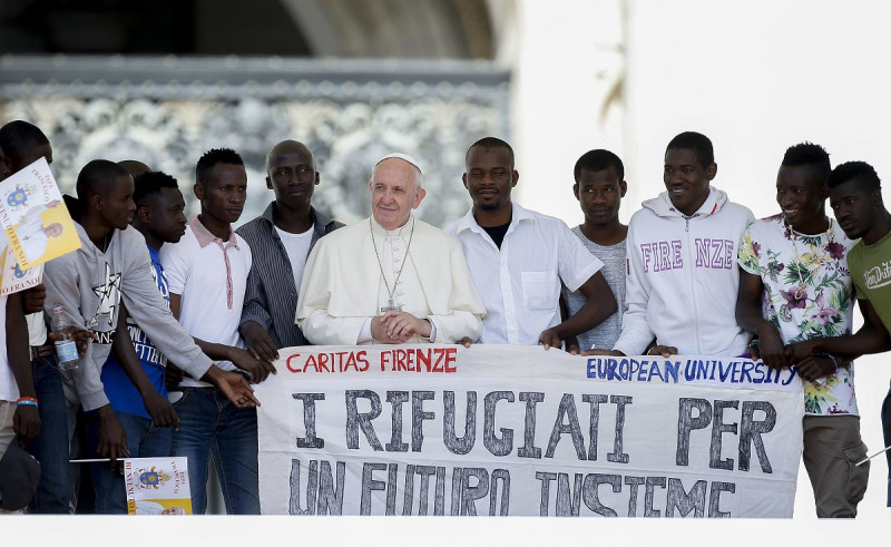 El papa Francisco posa para una fotografía con un grupo de refugiados a los que invitó a las escaleras de la Basílica de San Pedro, con una bandera con la frase (en italiano) "Los refugiados para un futuro junto", durante su audiencia general semanal, en la Plaza de San Pedro, en el Vaticano, el 22 de junio de 2016.