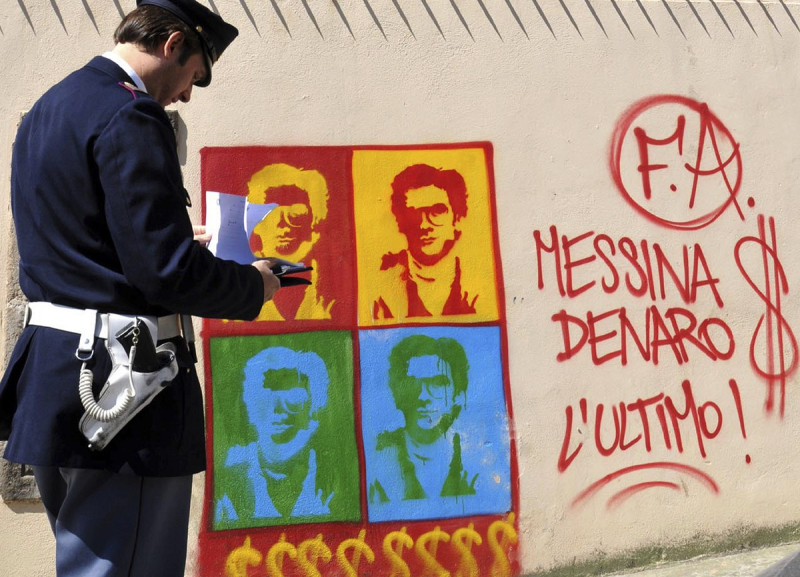 Un oficial de policía italiano observa un graffiti en el muro perimetral de la catedral de la ciudad de Palermo, retratando a Matteo Messina Denaro, en Sicilia, sur de Italia, el jueves 24 de abril de 2008.