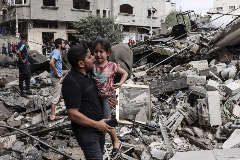 Un hombre lleva a un niño llorando mientras camina frente a un edificio destruido en un ataque aéreo israelí en la ciudad de Gaza el 7 de octubre de 2023