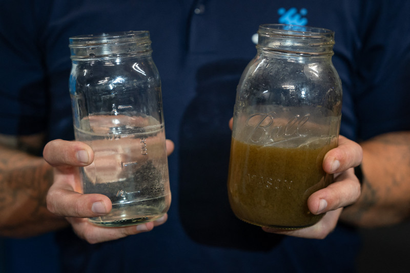 Ryan Pulley, director de operaciones de reutilización de agua para la startup Epic Cleantec, sostiene muestras de agua tratada y no tratada en el sótano de un edificio.
