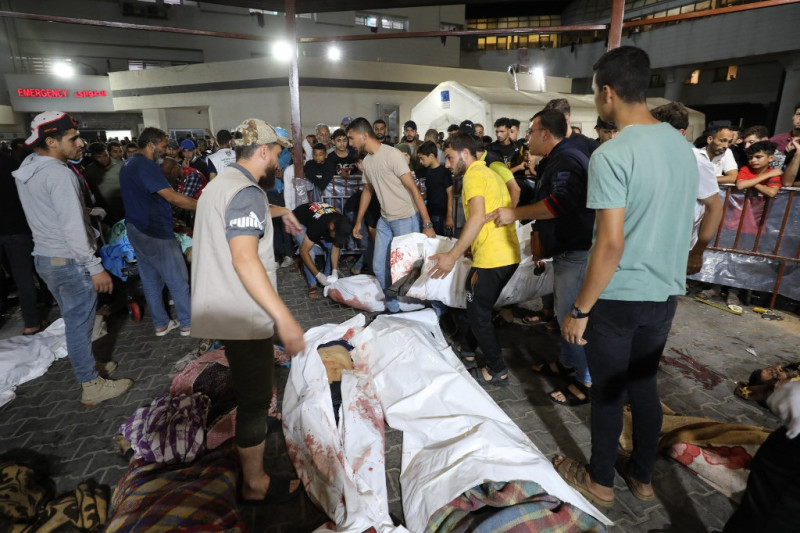 Varias personas se reúnen alrededor de los cuerpos de los palestinos muertos tras un ataque que arrasó el hospital Ahli Arab en el centro de Gaza, después de que fueran trasladados al hospital Al-Shifa, el 17 de octubre de 2023.