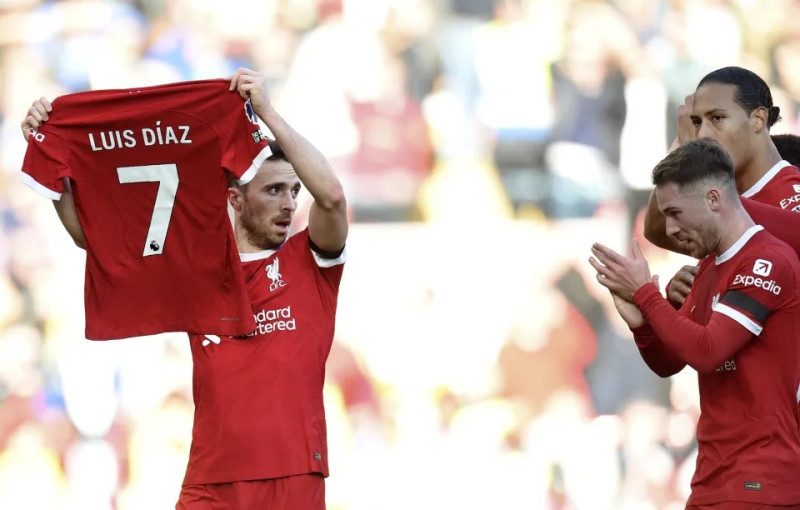 Un jugador del Liverpool muestra la chaqueta de su compañero Luis Díaz, mientras otros aplauden.