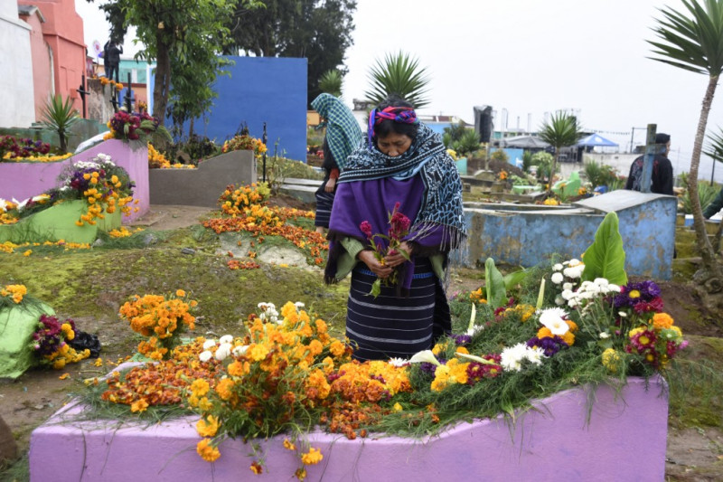 Una mujer indígena adorna la tumba de un familiar en el cementerio de Santiago Sacatepéquez