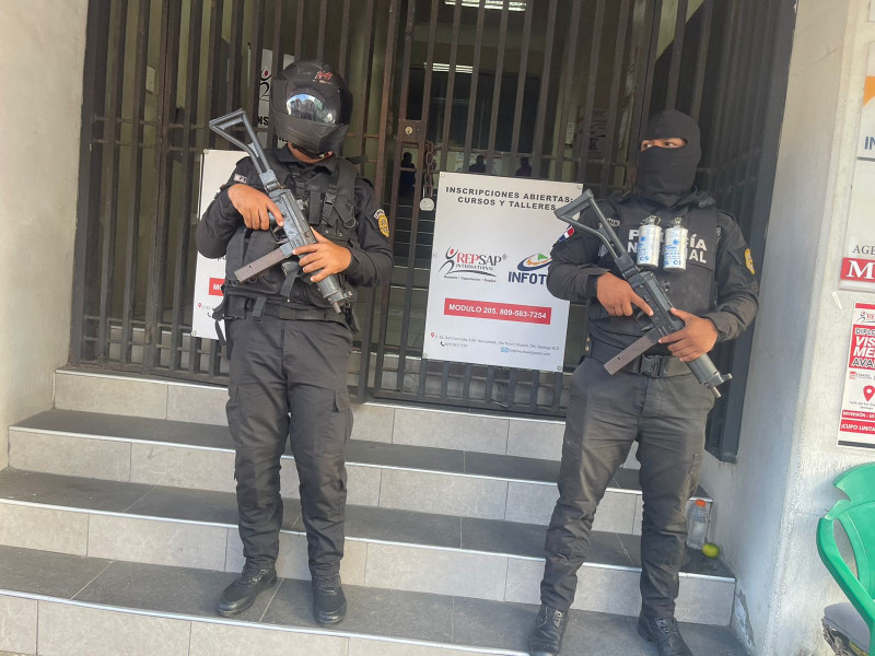 Elementos de la Policia Nacional custodian una puerta de un centro comercial, como parte de los allanamientos que se han realizado este jueves en Santiago.
