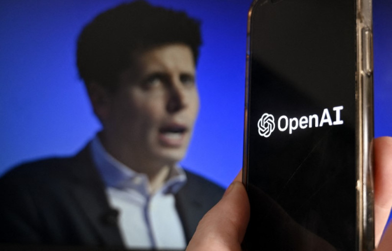 Esta foto muestra una pantalla de teléfono inteligente con el logotipo de OpenAI yuxtapuesto a una pantalla que muestra una foto del exCEO de OpenAI, Sam Altman