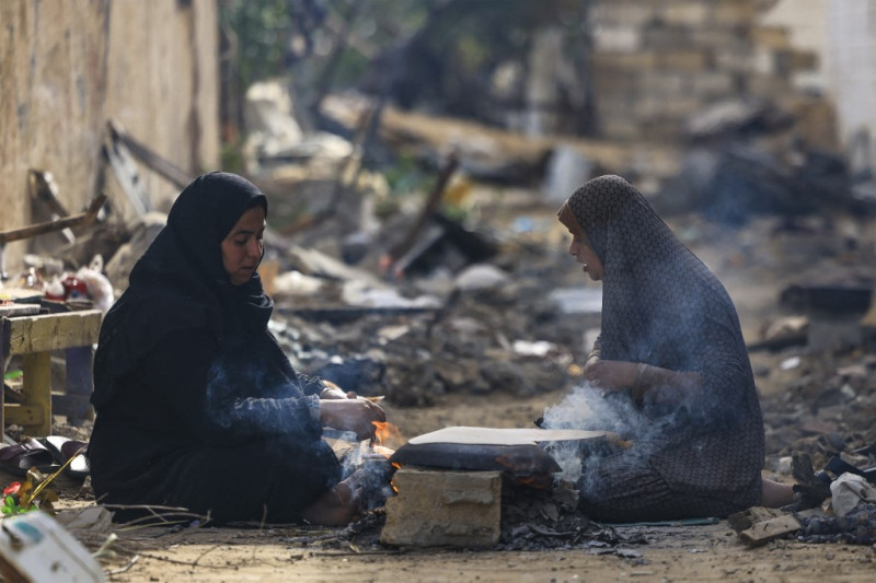 Mujeres palestinas preparan un horno de leña frente a sus casas dañadas en el distrito de Khezaa, a las afueras de la ciudad de Jan Yunis, en el sur de la Franja de Gaza, tras semanas de bombardeos israelíes