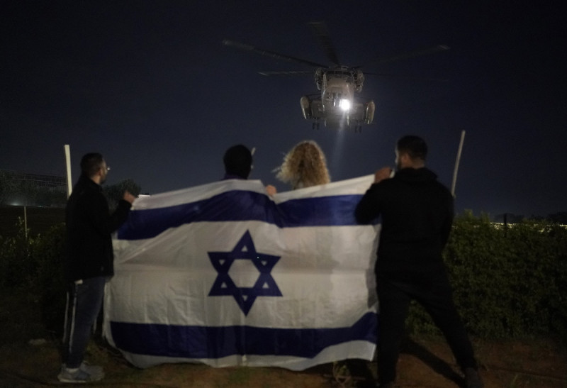 Gente sosteniendo una bandera israelí mira la llegada de un helicóptero que transporta a rehenes israelíes liberados por Hamás en el Centro Médico Sheba en Ramat Gan, Israel, el martes 28 de noviembre de 2023. Los mediadores internacionales trabajaban el miércoles 29 para ampliar la tregua en Gaza, con la esperanza de que Hamás, que gobierna el territorio, siguiera entregando rehenes a cambio de la liberación de prisioneros palestinos y más alivio de la ofensiva aérea y terrestre israelí. De lo contrario, el acuerdo expiraría en un día.