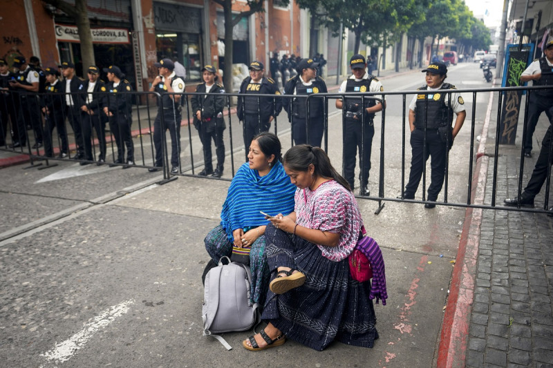 Un par de mujeres manifestantes se sientan frente a la policía cerca del edificio del Congreso en la ciudad de Guatemala, el martes 28 de noviembre de 2023.