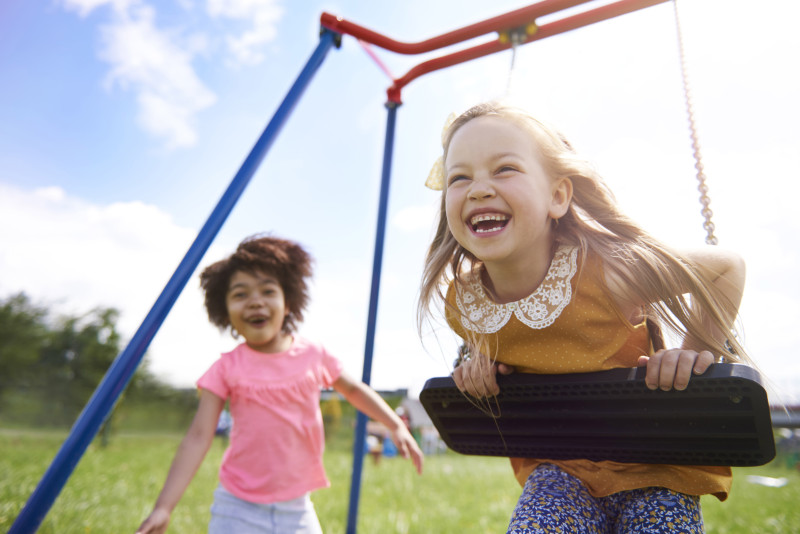 Dos niñas sonrientes juegan en un columpio en el parque. Foto: Open Comunicación.
