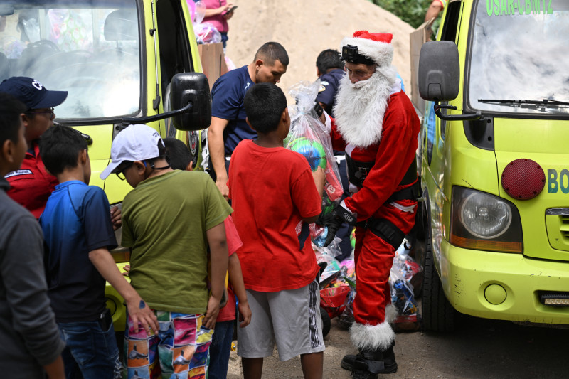 El bombero municipal guatemalteco Héctor Chacón, vestido como Papá Noel, entrega regalos a los niños después de bajar por un cable desde un puente en la ciudad de Guatemala el 17 de diciembre de 2023.