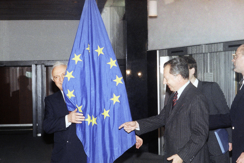El ministro soviético de Asuntos Exteriores, Eduard Shevardnadze, se asoma por detrás de la bandera de la Unión Europea, mientras el presidente de la Comisión Europea, Jacques Delors, señala el lugar donde debería estar de pie.