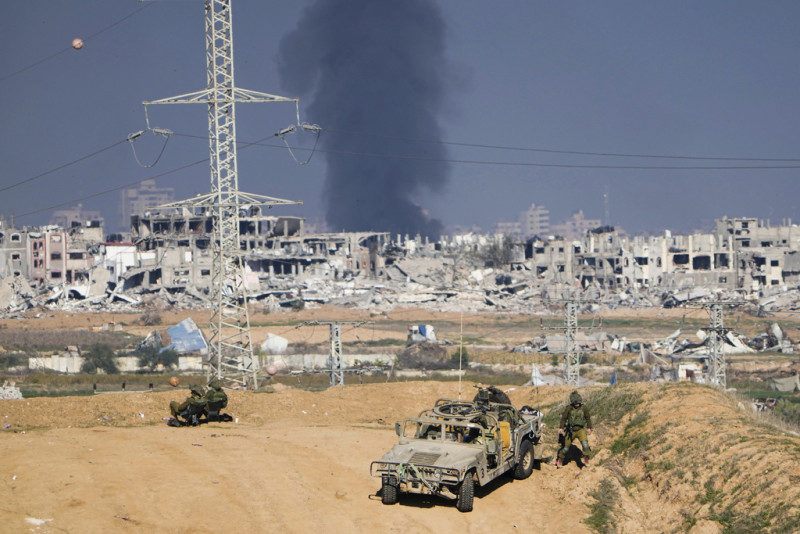 Soldados israelíes toman posiciones cerca de la frontera de la Franja de Gaza, mientras al fondo una columna de humo marca el lugar donde se produjo un ataque aéreo israelí