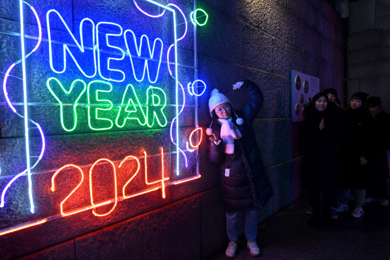 A woman poses for a photo in front of a 2024 luminous sign before a countdown event to celebrate the New Year in central Seoul on December 31, 2023. (Photo by Jung Yeon-je / AFP)