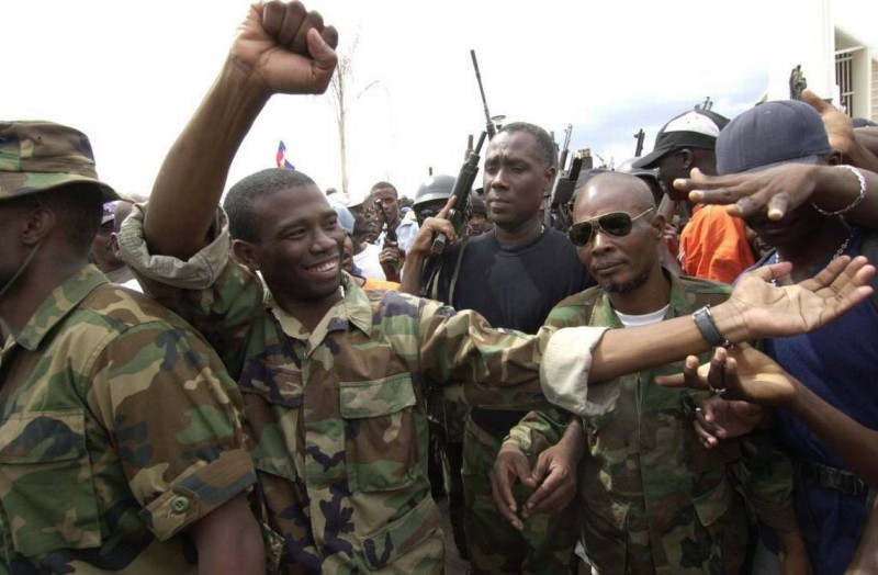 A la izquierda, Guy Philippe, el exlíder militar golpista haitiano que el pasado sábado anunció su intención de entrar con sus fuerzas a la capital, Puerto Príncipe, con planes de derrocar al gobierno.