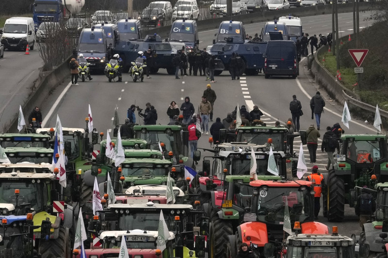 Tractores colocados ante vehículos de las fuerzas de seguridad en una autopista cortada, el miércoles 31 de enero de 2024 en Chilly-Mazarin, en el sur de París.