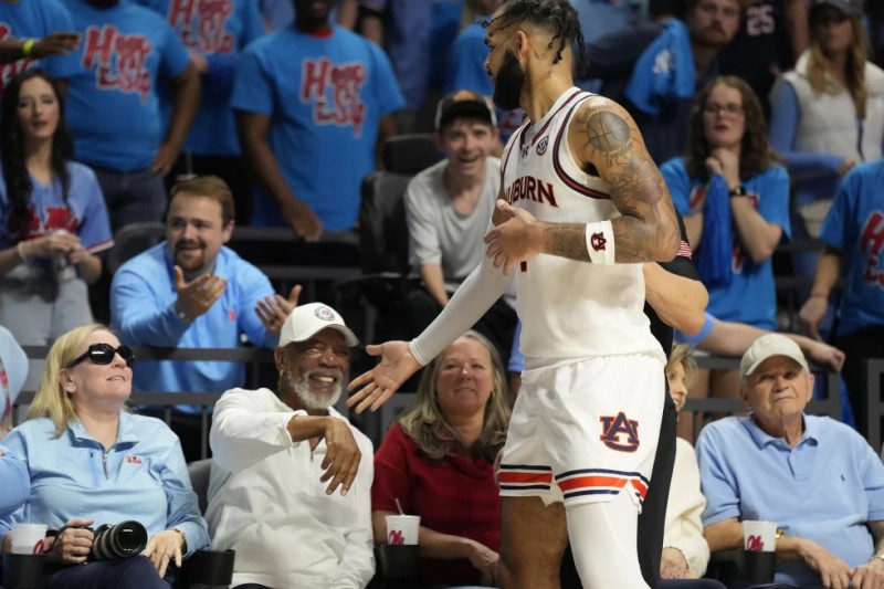 El alero de Auburn, Johni Broome, al frente a la derecha, extiende la mano y se disculpa con el actor ganador del Premio de la Academia y fanático de Mississippi Morgan Freeman, segundo desde el frente a la izquierda, después de caer sobre él mientras perseguía el balón.