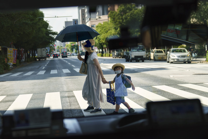 Una mujer cruza la calle con un niño, vista a través de la ventana de un taxi en Tokio el lunes 19 de julio de 2021.