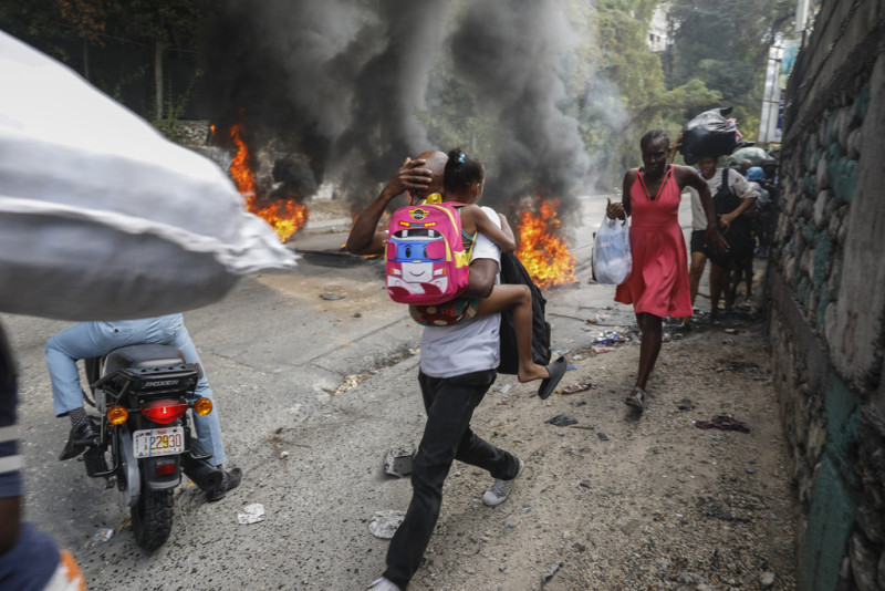 Varias personas corren junto a neumáticos en llamas durante una protesta contra el primer ministro Ariel Henry, el lunes 5 de febrero de 2024, en Puerto Príncipe, Haití.