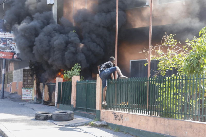 Un hombre sube la valla de una oficina de la compañía eléctrica de Haití incendiada durante una protesta para exigir la renuncia del primer ministro Ariel Henry en Puerto Príncipe, Haití.