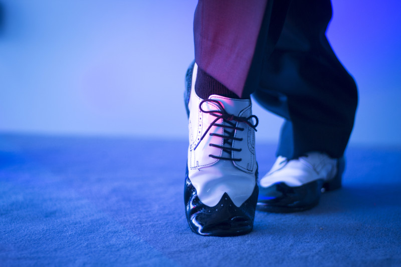 Male latin and salsa dancer in black and white jazz dancing shoes in light and dark on stage.