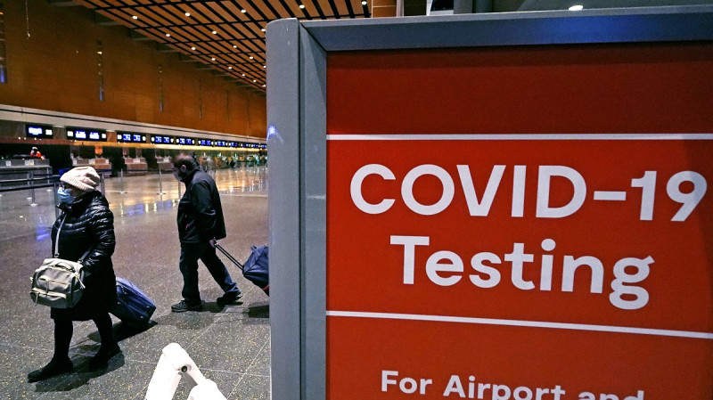Viajeros pasan junto a un letrero cerca de un centro de pruebas de COVID-19 en la Terminal E del aeropuerto Logan el 21 de diciembre de 2021, en Boston.