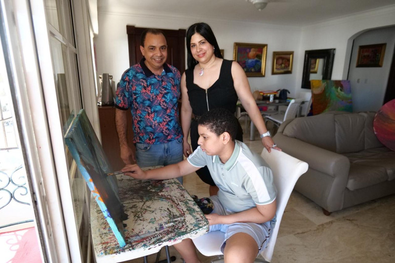 Fotografía muestra al niño Fernando Gabriel Quiroz Flaviá junto a sus padres mientra pinta uno de los cuadros de la exposición Multiverso de Colores.