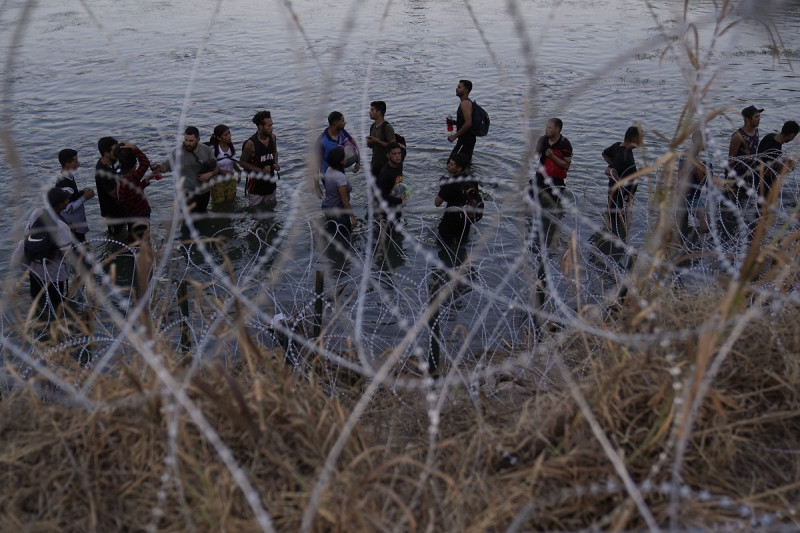 Migrantes esperan para trepar por encima del alambre de púas después de cruzar el Río Bravo y entrar en Estados Unidos desde México, el 23 de septiembre de 2023 en Eagle Pass, Texas.