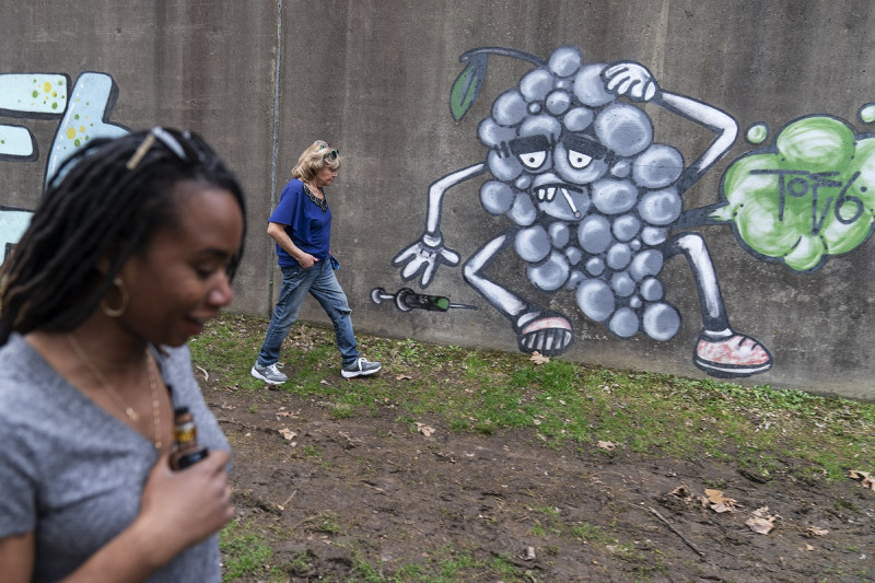 Larrecsa Cox, en primer plano, y Sue Howland caminan frente a un grafiti con temática de adicciones de drogas cerca de un campamento en Huntington, Virginia Occidental, el 17 de marzo de 2021.