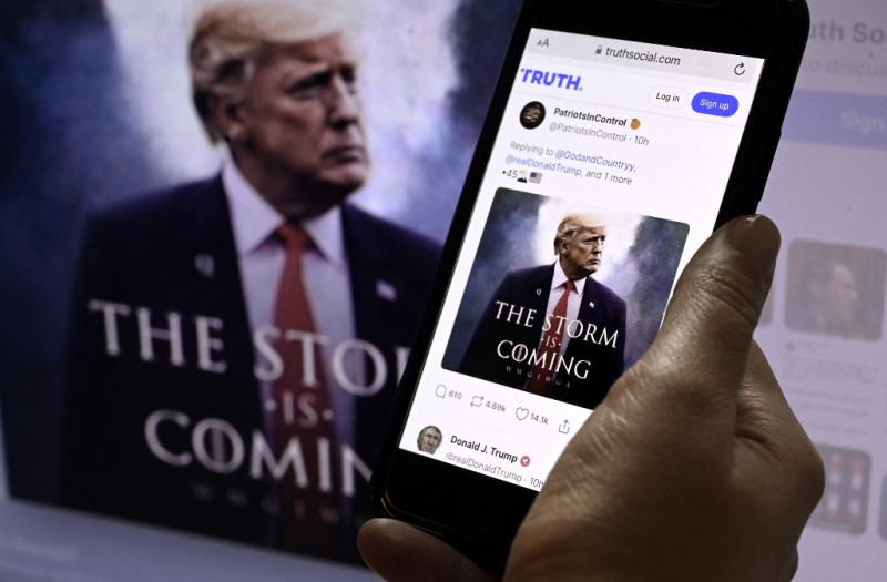 En esta ilustración fotográfica, la cuenta TRUTH Social del expresidente estadounidense Donald Trump en un dispositivo móvil con una imagen de Trump de fondo