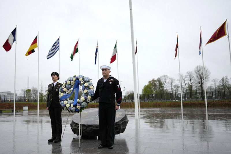 Dos militares se ven bajo las banderas de los estados miembros de la OTAN durante una ofrenda floral en la sede de la alianza en Bruselas, el jueves 4 de abril de 2024.