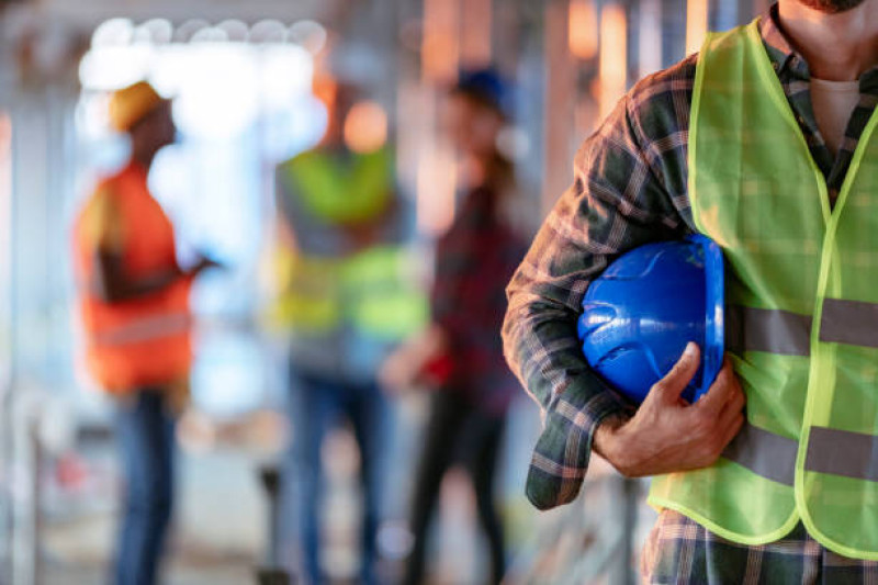 Hombre sujetando casco azul de cerca. Trabajador de la construcción con oficina y gente en segundo plano.