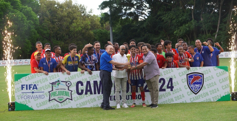 José Frank Acosta, secretario de Fedofútbol, y el viceministro Técnico de Miderec, Elvis Duarte, entregan la copa de campeón a Ender Segura, capitán de los Delfines y al padre Eulogio Castaños.