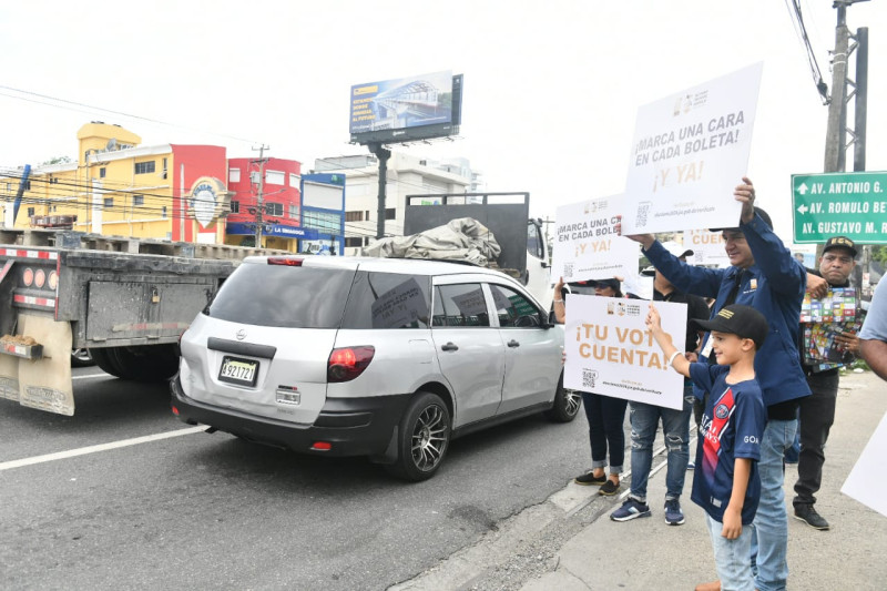 Miembros de la Junta Central Electoral sosteniendo pancartas en las calles para motivar a los capitaleños a ejercer el derecho al voto en las elecciones congresuales y presidenciales del 19 de mayo.