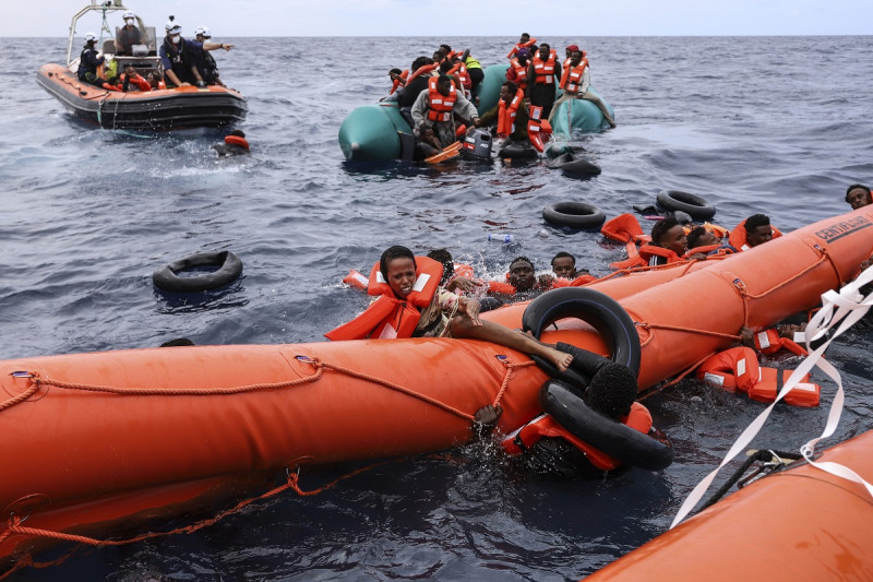 Migrantes que viajaban en una lancha de goma caen al agua mientras otros se aferran a una boya antes de ser rescatados por un equipo del barco Sea Watch-3, a unas 35 millas de la costa Libia, el lunes 18 de octubre de 2021.