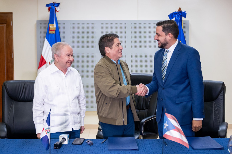 Iván Ruiz y Jorge Pagán se saludan tras la firma del acuerdo entre RTVD y  WIPR TV. A la izquierda, figura Ellis Pérez.
