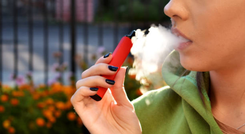 Fotografía muestra mujer fumando cigarrillo electrónico en lugar público.