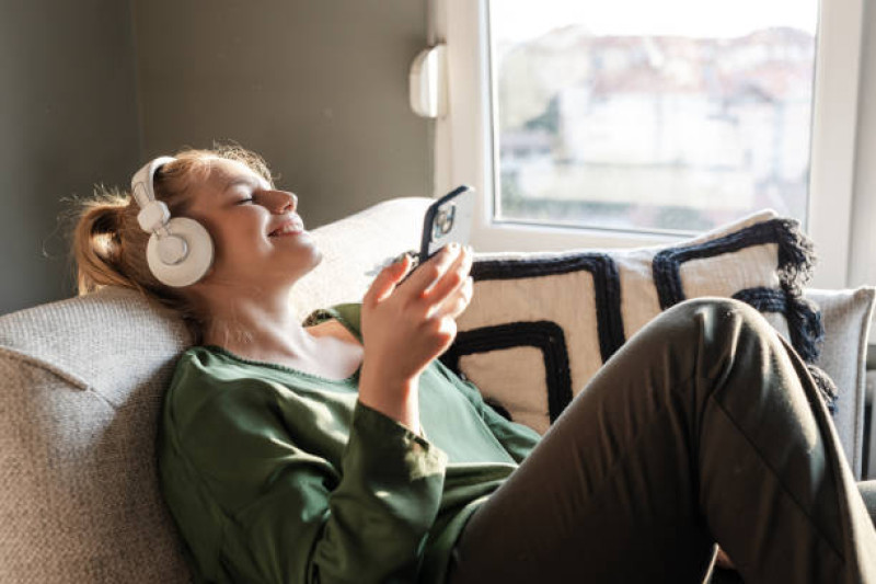 Mujer joven relajándose en un sofá y escuchando música en su teléfono a través de auriculares.