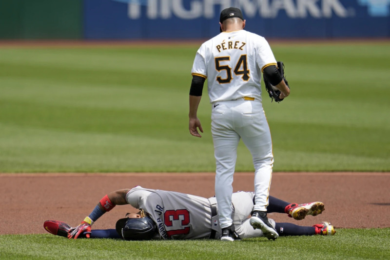 Ronald Acuña Jr. se retuerce del dolor mientras es contemplado por el también venezolano Martín Pérez, lanzador de Pittsburgh.