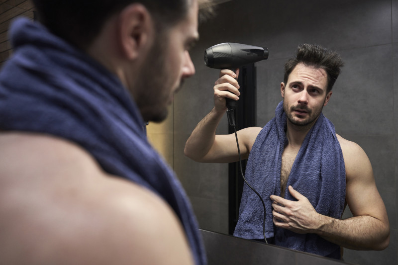 Hombre secándose el pelo ante un espejo en el baño. Foto: Hospital Capilar.