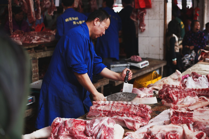 Fotografía muestra a carnicero cortando carnes de cerdo.