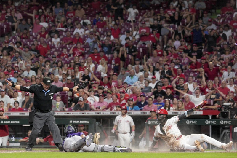 Elly De La Cruz, derecha, de Cincinnati, reacciona después de evitar un toque del receptor de los Rockies, Elias Díaz, centro, y anotar en jugada de opción.