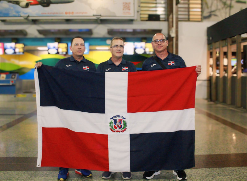 El tirador Eduardo Lorenzo sostiene la bandera dominicana, junto a su entrenador Pedro Zayas, y el psicólogo, Jorge López.
