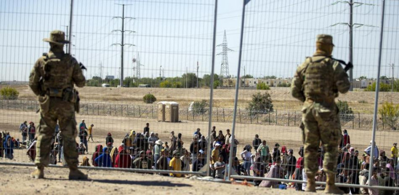 Varios migrantes esperan junto a la cerca fronteriza ante la mirada de guardias nacionales de Texas para entrar en El Paso, TexasANDRES LEIGHTON