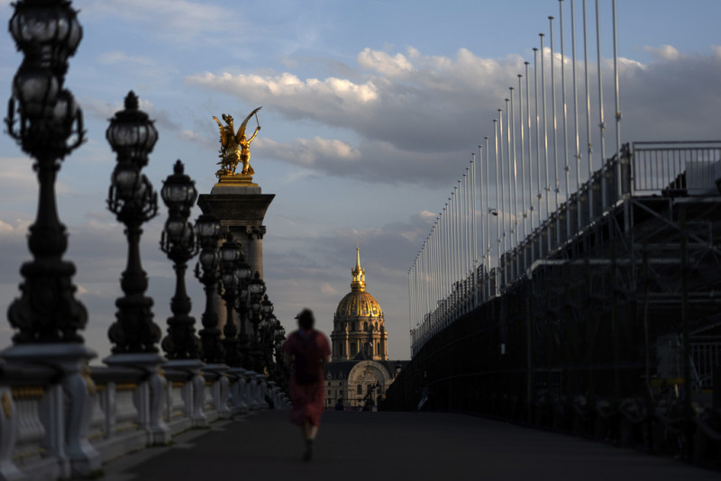 La puesta del sol frente al Hotel de los Inválidos mientras una persona cruza el puente Alexander III sobre el río Sena, el viernes 19 de julio de 2024